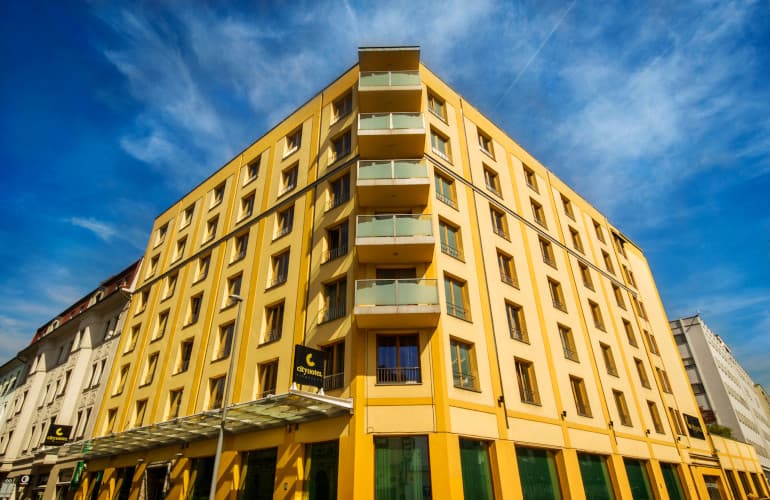 Yellow Cityhotel building exterior with balconies under a bright blue sky in Ljubljana.