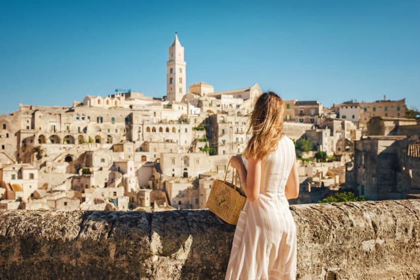 Woman tourist enjoying panoraming view of Matera city in Italy.Young woman in romantic dress and handbag standing against the backdrop of ancient city of Matera in Italy