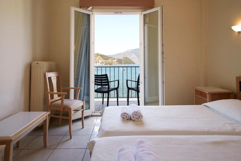 Hotel room with twin beds and balcony overlooking a bay with mountains and boats.