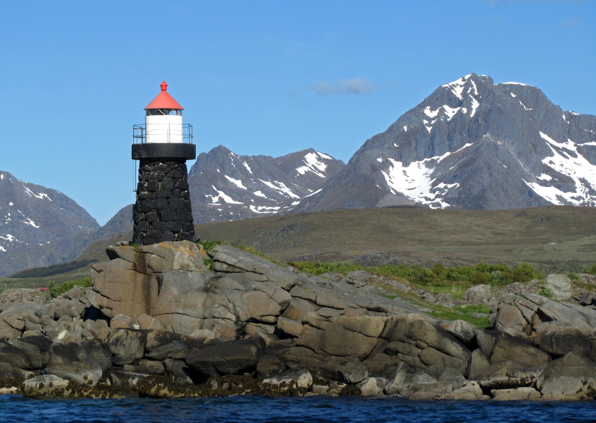 lighthouse, birds on the rocks, and snowy mountains on a sunny day near leknes in the lofoten islands, nordland, norway