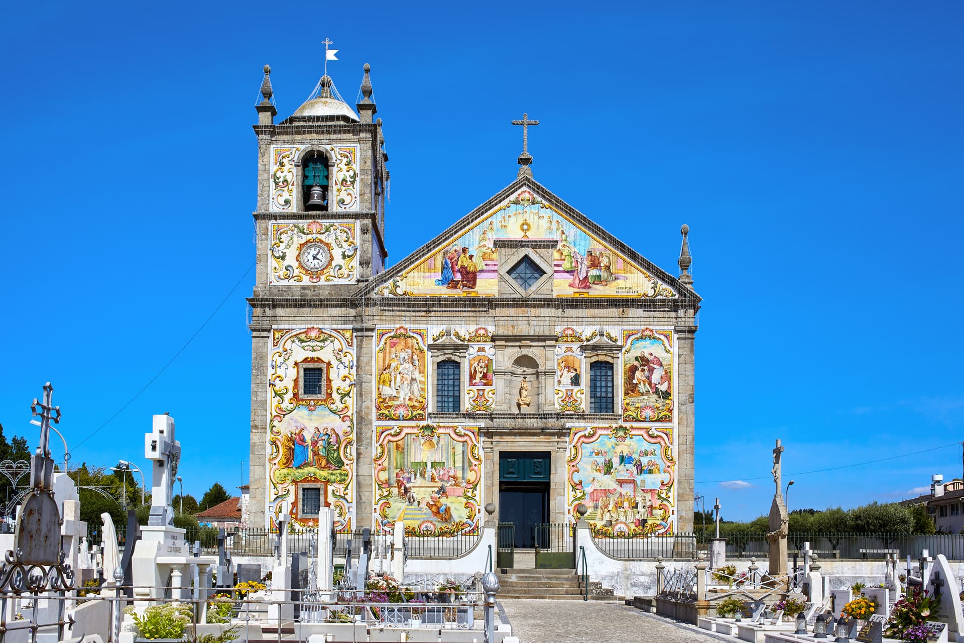 Church in Ovar with colorful tile facade and adjacent cemetery under bright blue sky.