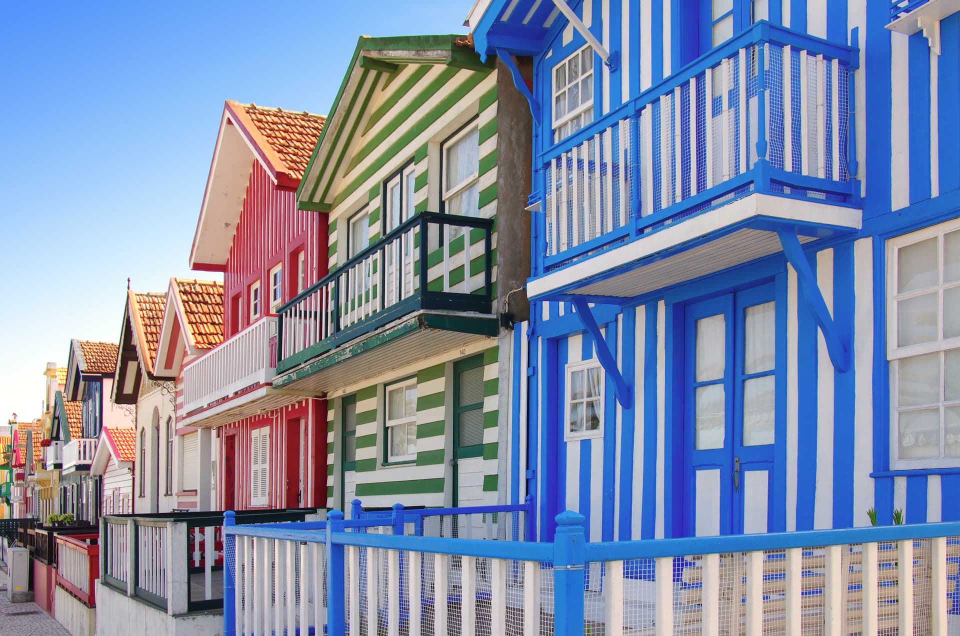 Colorful striped beach houses with balconies under a clear blue sky in Costa Nova.