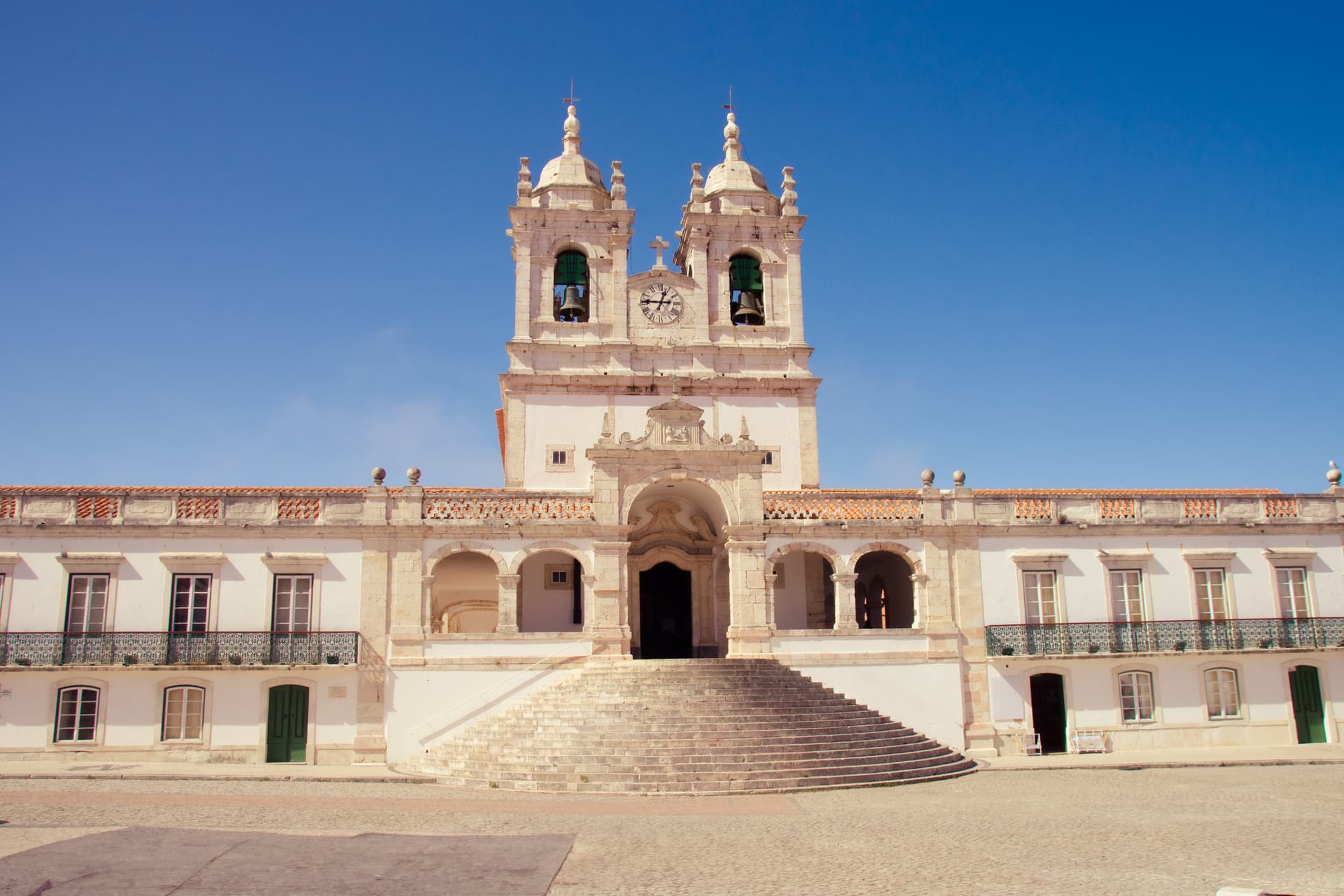 Baroque church facade with twin bell towers and wide stone steps under a clear blue sky.