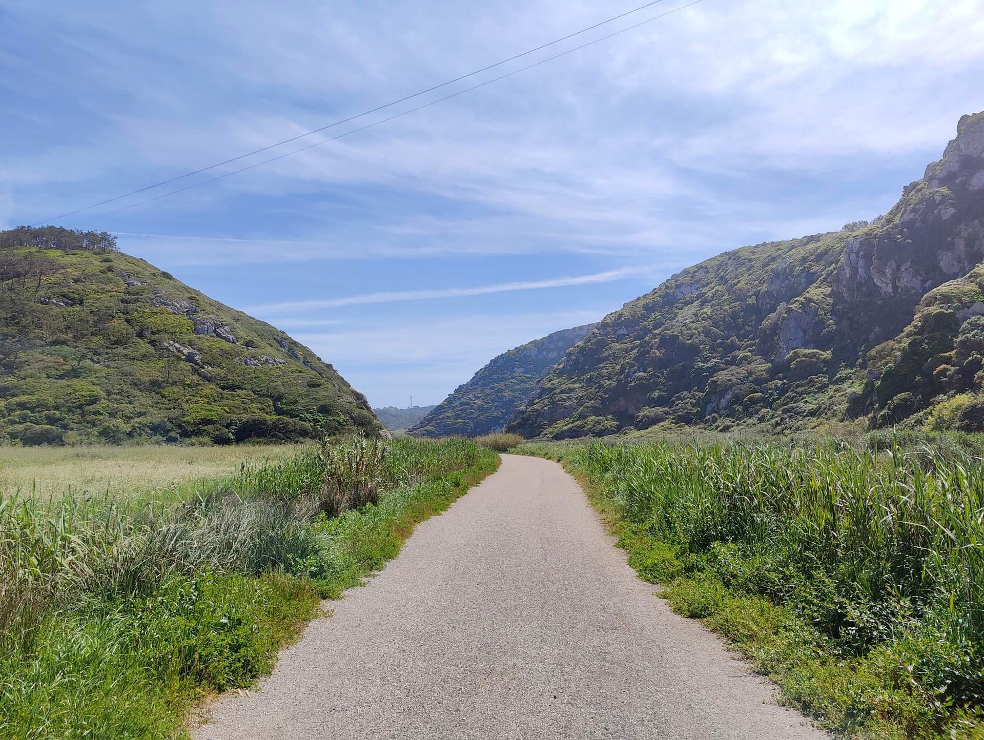 Gravel path cycling through a valley between green, scrub-covered hills under a blue sky