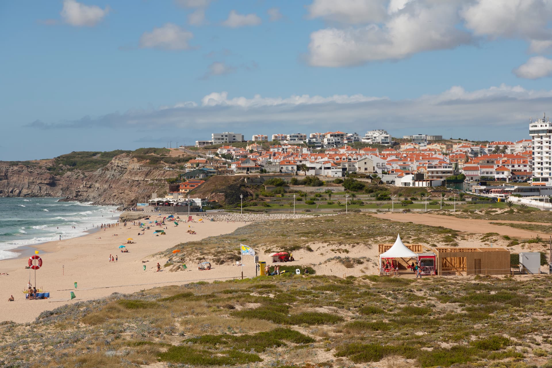 Beachgoers at Praia da Areia Branca with white buildings on coastal cliffs.
