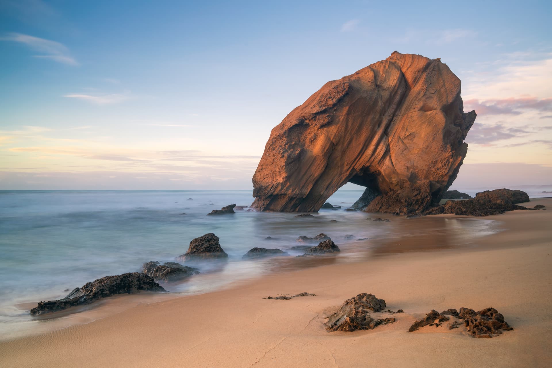 Praia de Santa Cruz beach rock arch at sunset with smooth ocean water and golden sand.