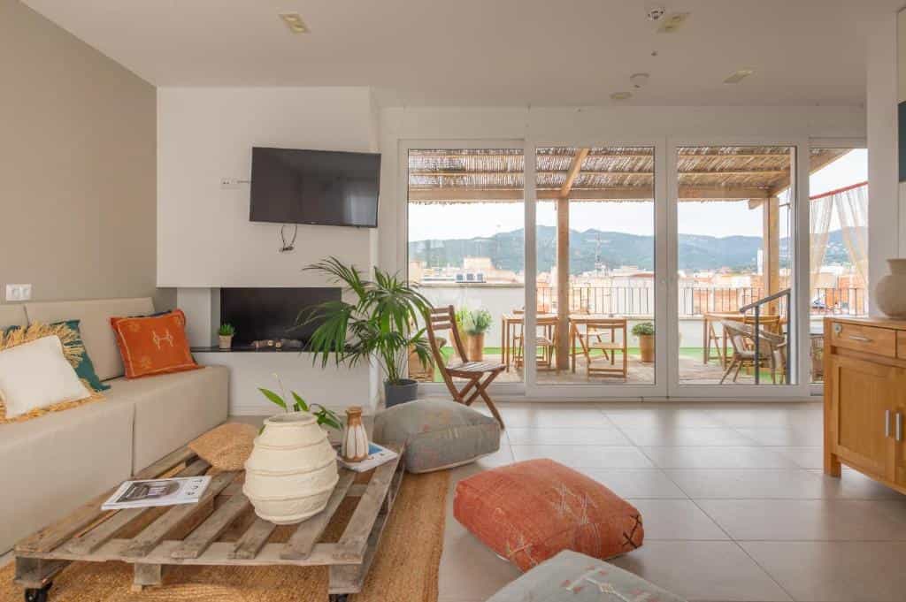 Modern living room with pallet coffee table, sofa, and terrace overlooking a town with mountains in the background.