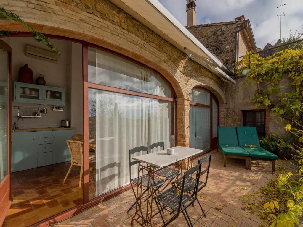 Patio with metal table, chairs, and lounge chairs outside a rustic stone building with arched glass doors.