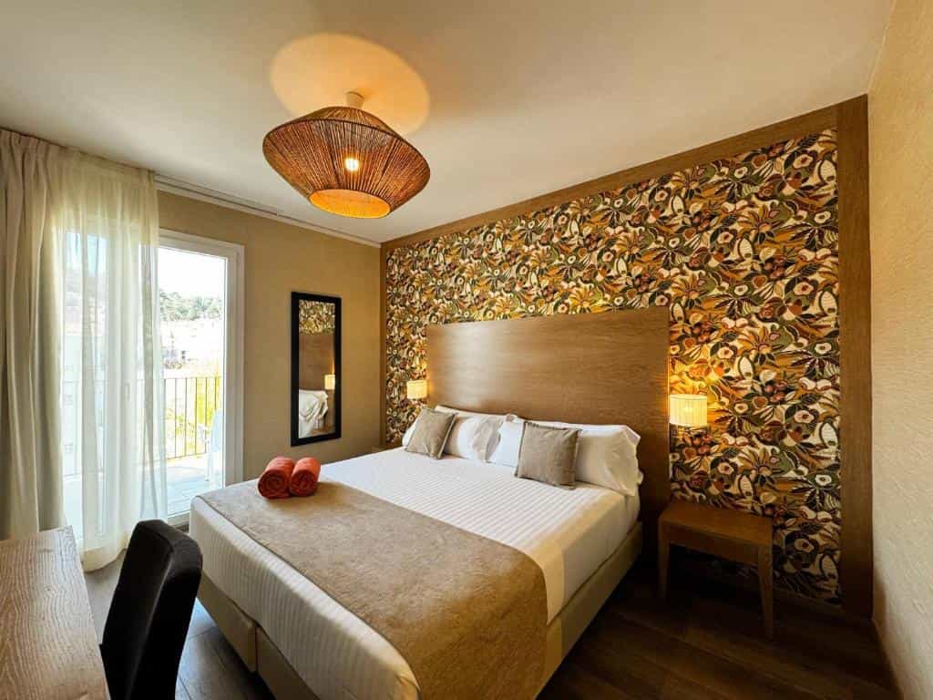 Hotel bedroom with double bed, floral accent wall, and balcony access.