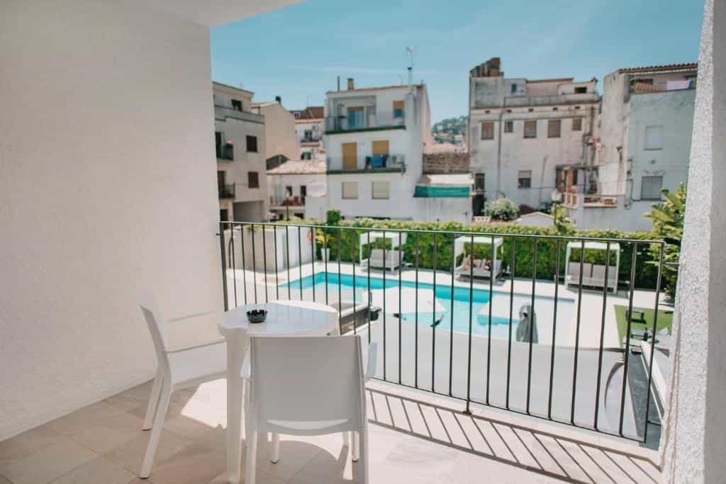 Balcony with table and chairs overlooking a swimming pool in a town setting.