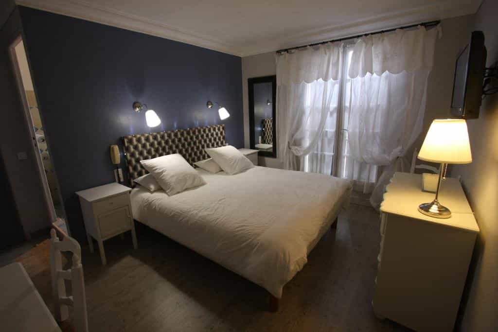 Hotel bedroom with a double bed, white linens, bedside lamps, and sheer curtains.