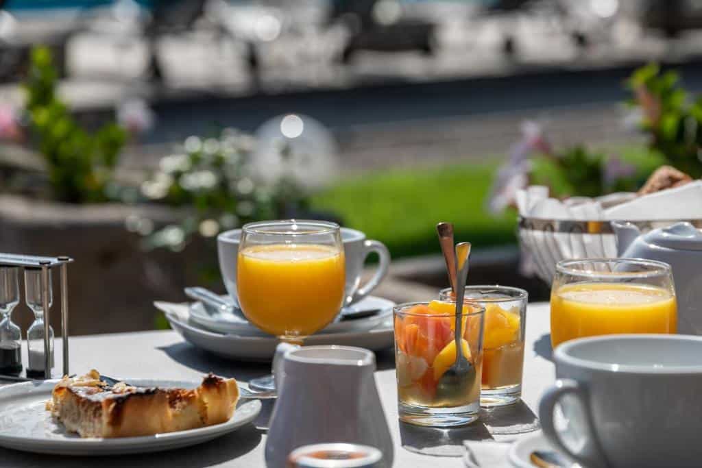 Breakfast table with orange juice, fruit cups, and pastry outdoors.