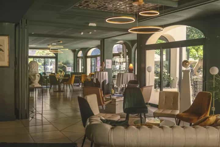 Elegant hotel lounge interior with modern velvet armchairs, circular pendant lights, and arched windows.