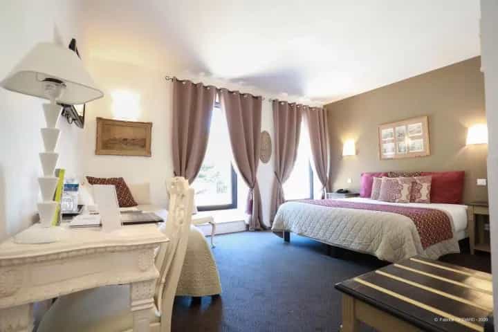 Hotel room with a bed, desk, white lamp, and curtains covering windows.