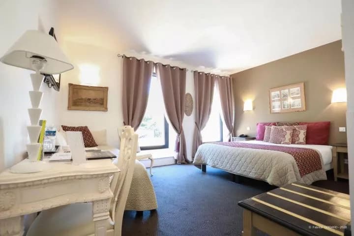 Hotel room with a bed, desk, white lamp, and curtains covering windows.