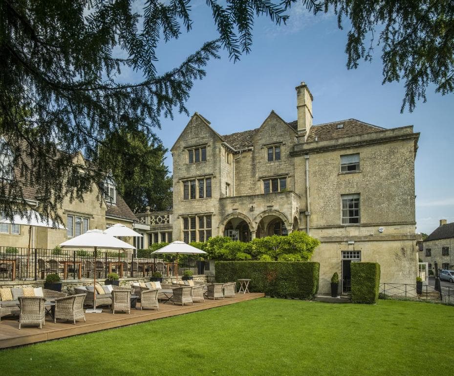 Historic stone manor house with outdoor patio seating and green lawn.