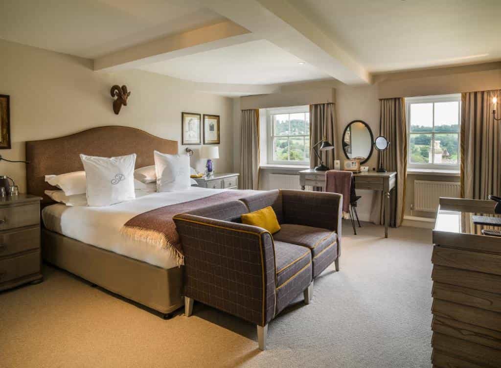 Hotel bedroom with a king-sized bed, plaid sofa, vanity desk, and windows overlooking a green landscape.