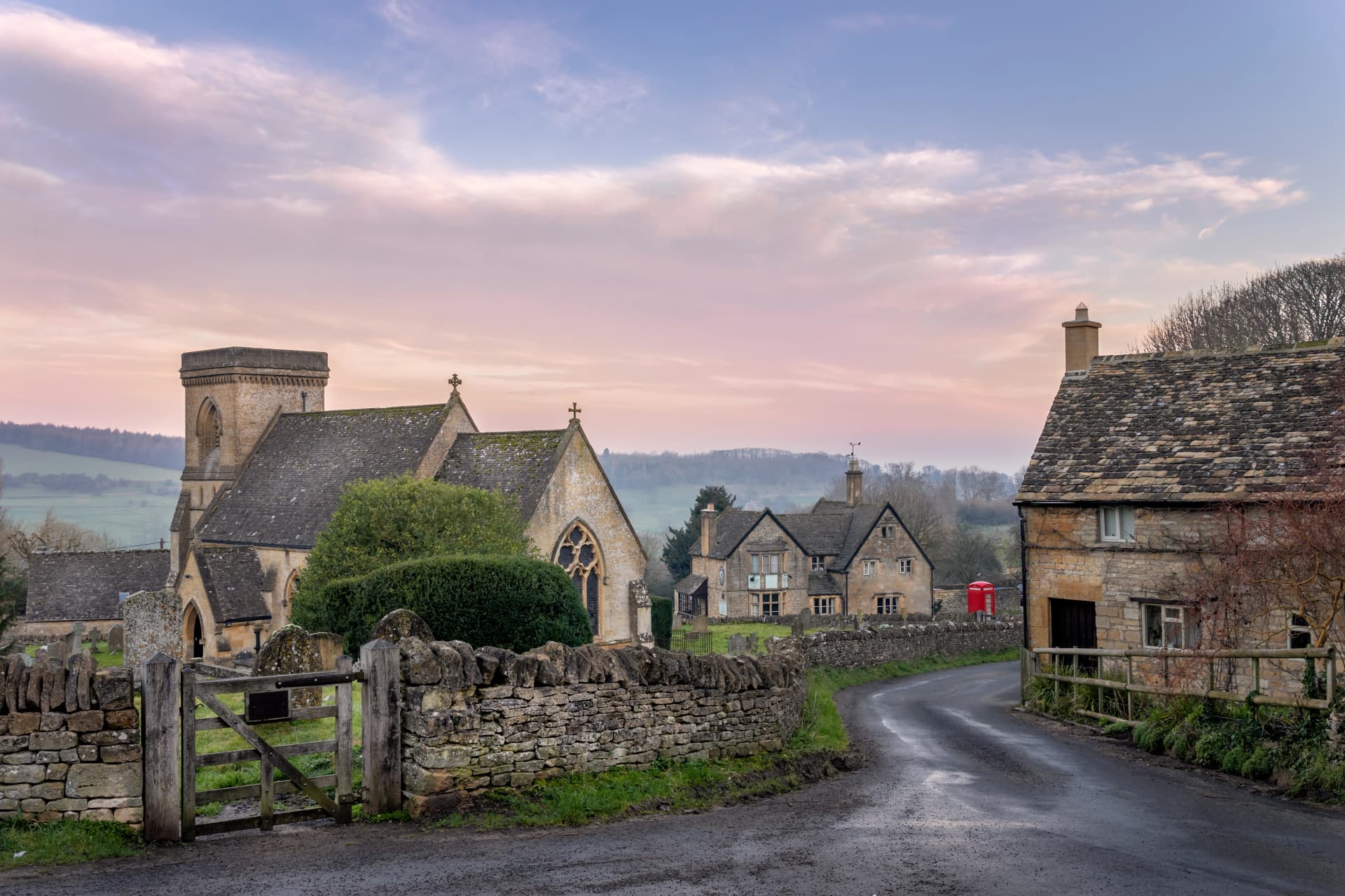 Snowshill church in the Cotswolds gloucestershire with lane leading past a cottage towards red telephone box and country pub