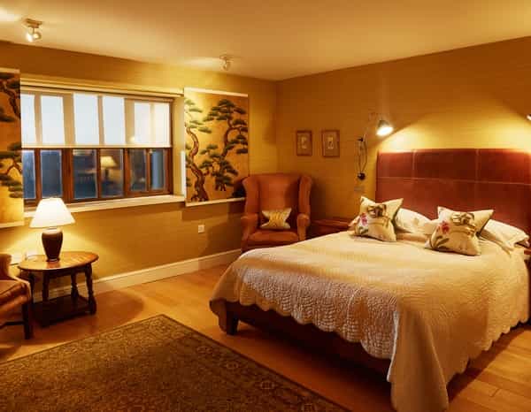 Hotel bedroom with a double bed, armchair, side table, and warm lighting.