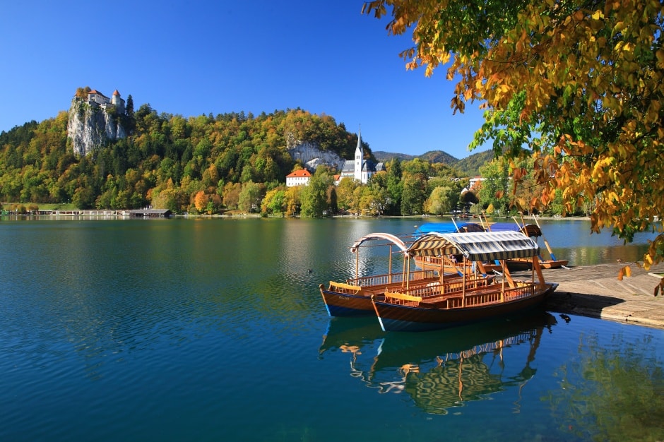 Traditional wooden pletna boats on Lake Bled, Slovenia, with Bled Castle on the cliff and autumn foliage.