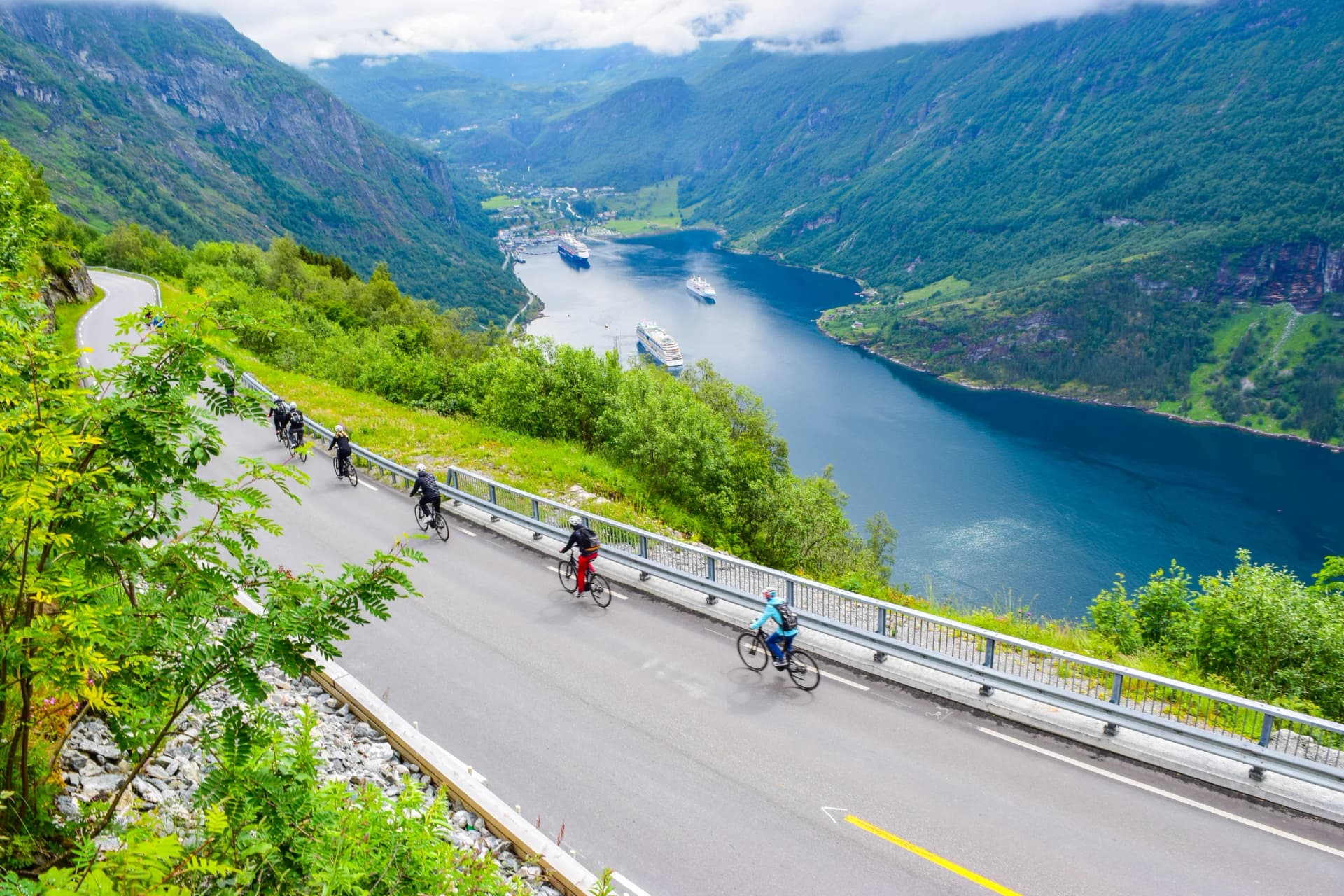 The cruise liners at the end of Geirangerfjord, near small village of Geiranger. Group of cyclists riding down Eagles Road. Norway.