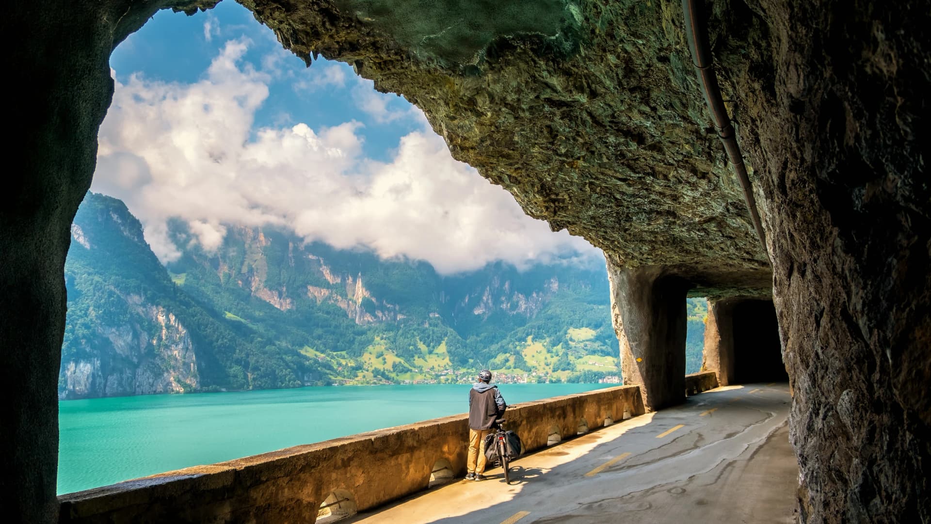 A 55-year-old man stops in a tunnel in Switzerland and admires, through rock windows, the magnificent scenery of the shores of Lake Lucerne and the mountains during his bike ride on holiday.