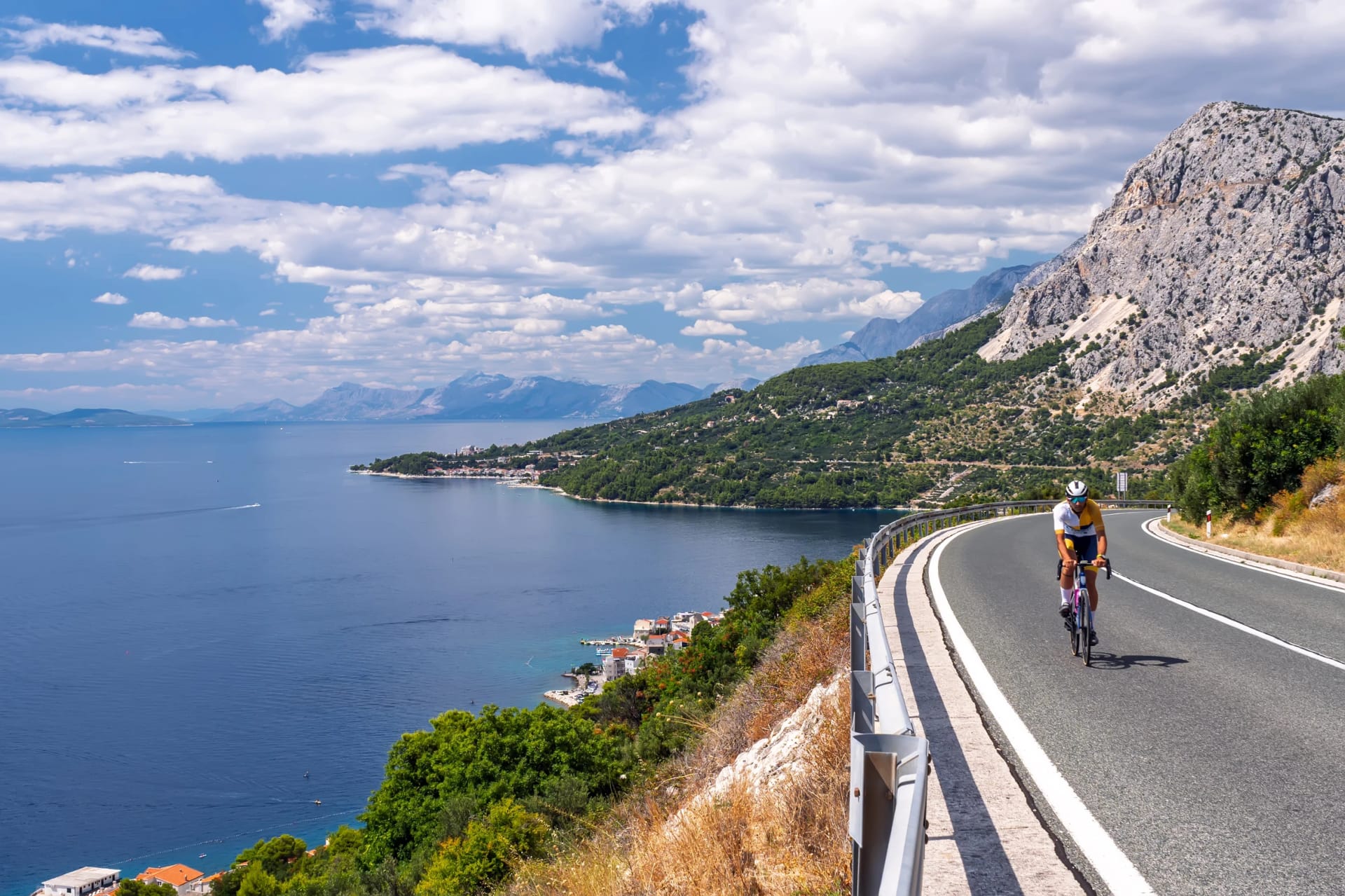 Capturing the essence of a perfect active vacation: a cyclist pedaling along a high-altitude road with incredible, expansive views of the sparkling sea and picturesque shoreline.Active Holiday