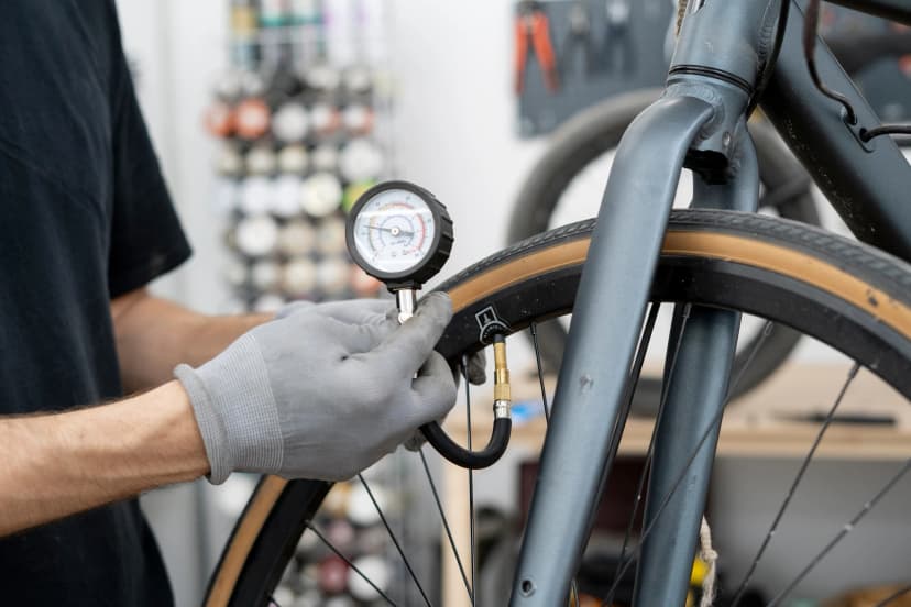 A person is adjusting the tire pressure of a bicycle using a hand-held gauge. The setting is a well-equipped bike shop