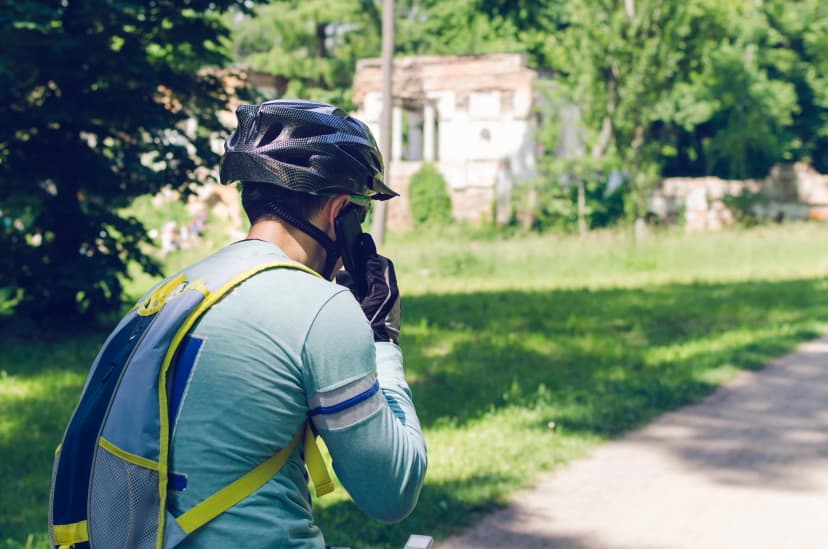 A cyclist in a helmet is riding in the park and talking on the phone