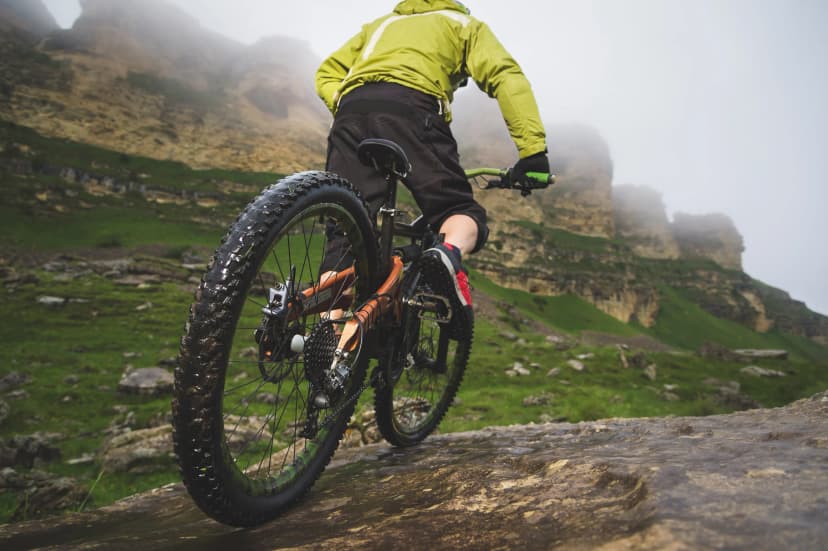 Legs of bicyclist and rear wheel close-up view of back mtb bike in mountains against background of rocks in foggy weather. The concept of extreme sports