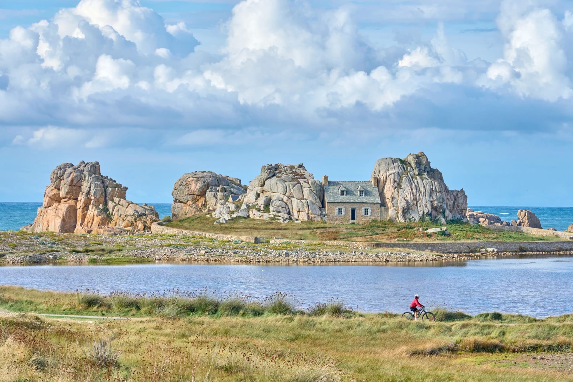 nice senior woman cycling with her electric mountain bike at the rocky rose granite coast of Le Gouffre de Plougrescant, Brittany, France