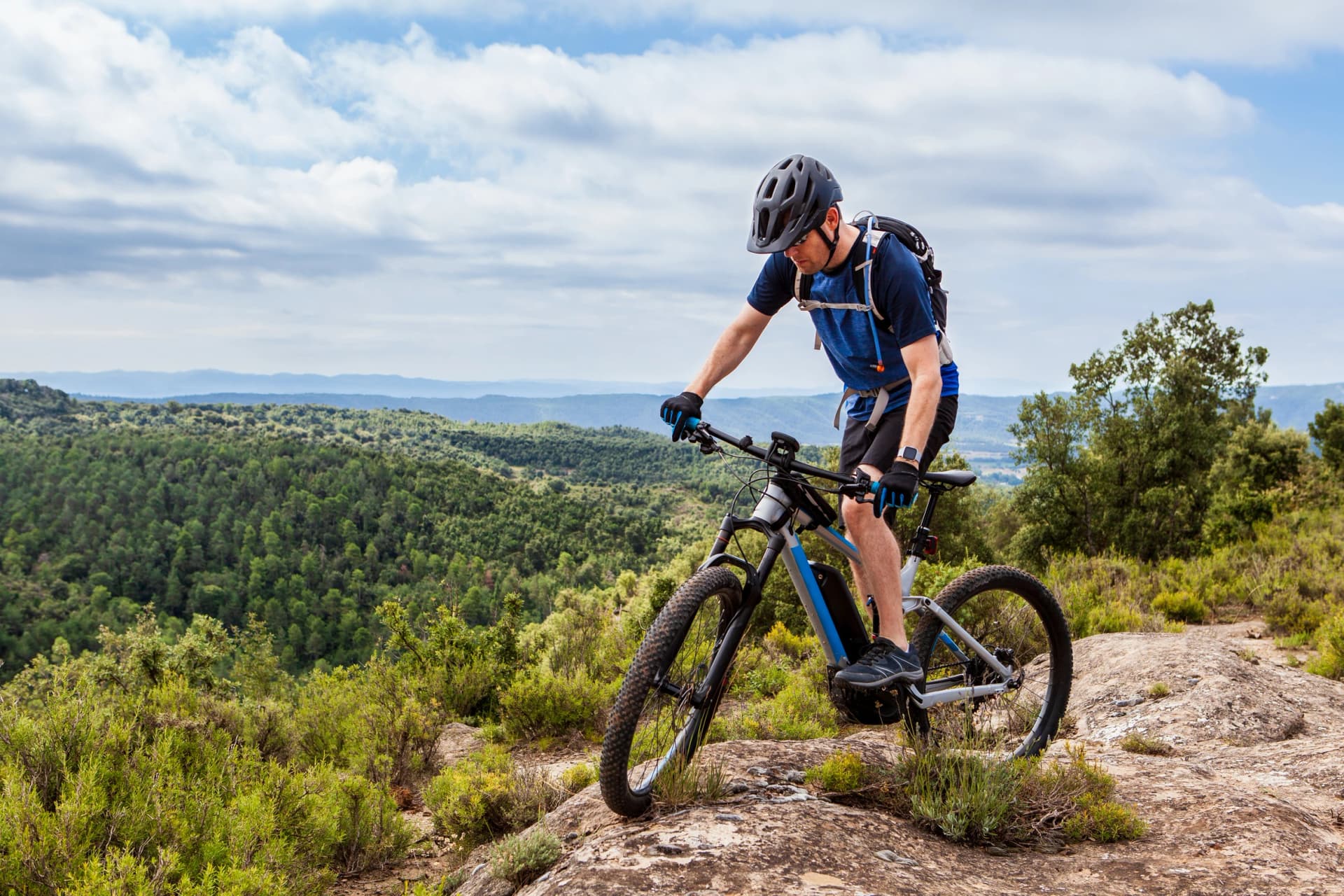 Male mountain biker balancing his ebike on a rock, nice landscape in the background