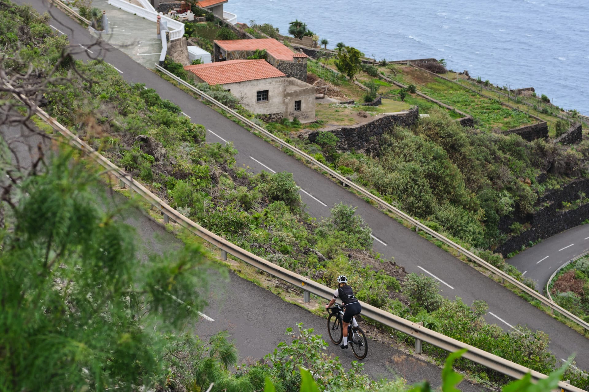 Top view of woman cyclist riding a road bike with a view of the mountains and ocean. Cycling adventure. Female cyclist wearing a cycling kit and helmet. Tenerife, Canary Island, Spain. Curvy road.