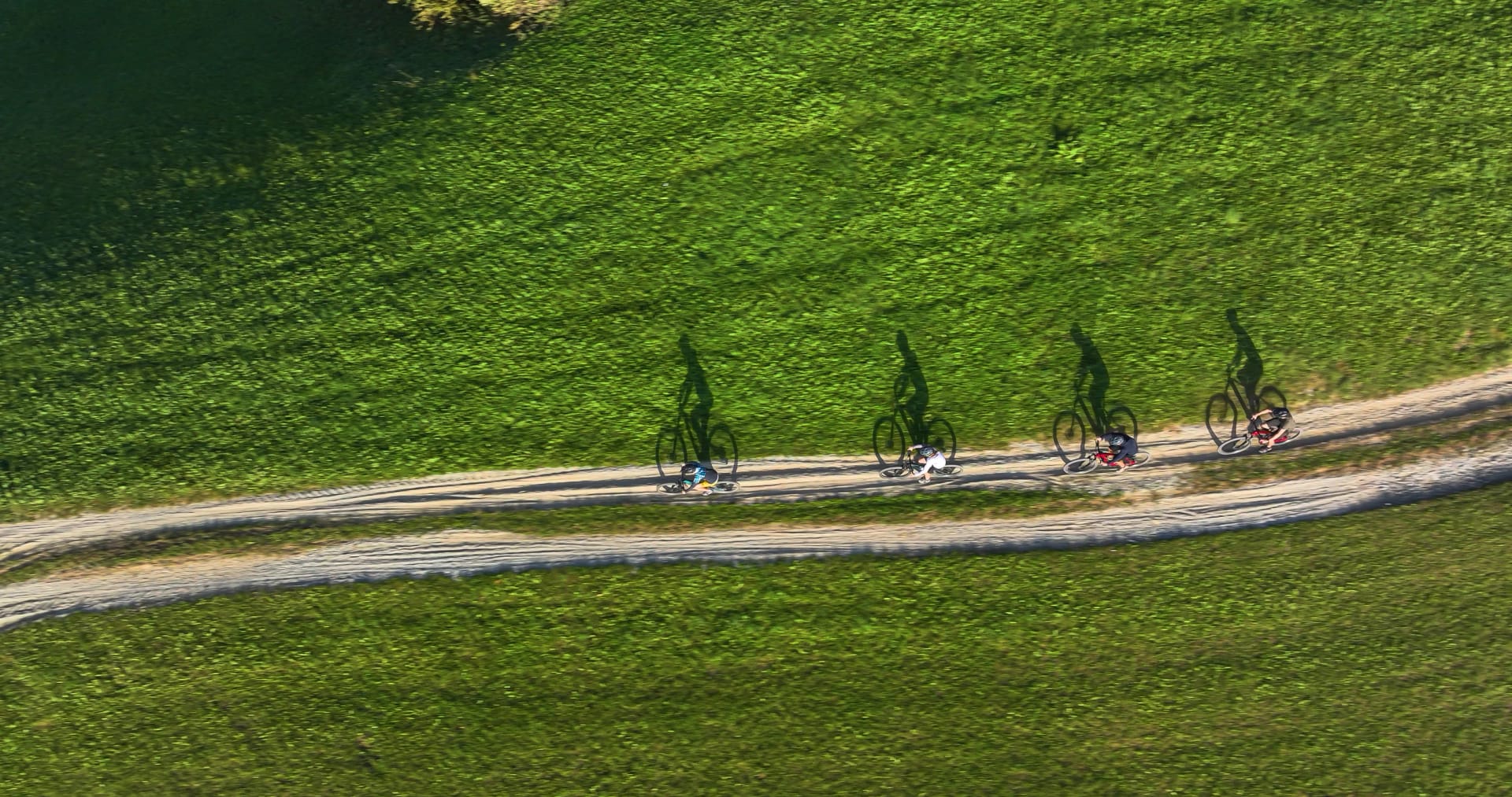 AERIAL, TOP DOWN: A group of friends ride their mountain bikes along a set of gravel tracks in the idyllic green hills of Slovenia. Active tourists ride their e-bikes across the scenic countryside.