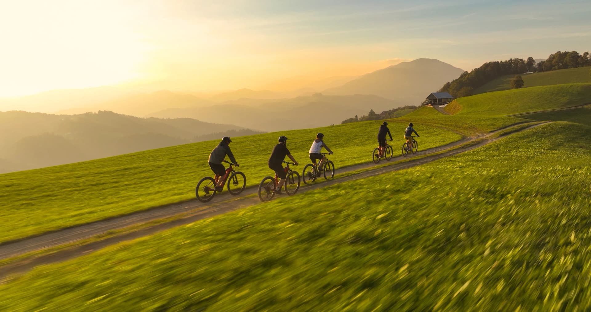 AERIAL: Biking friends on a scenic bike ride through hilly Slovenian countryside. Group of young mountain bikers riding along a hilltop mountain trail with breathtaking views on sunny autumn morning.