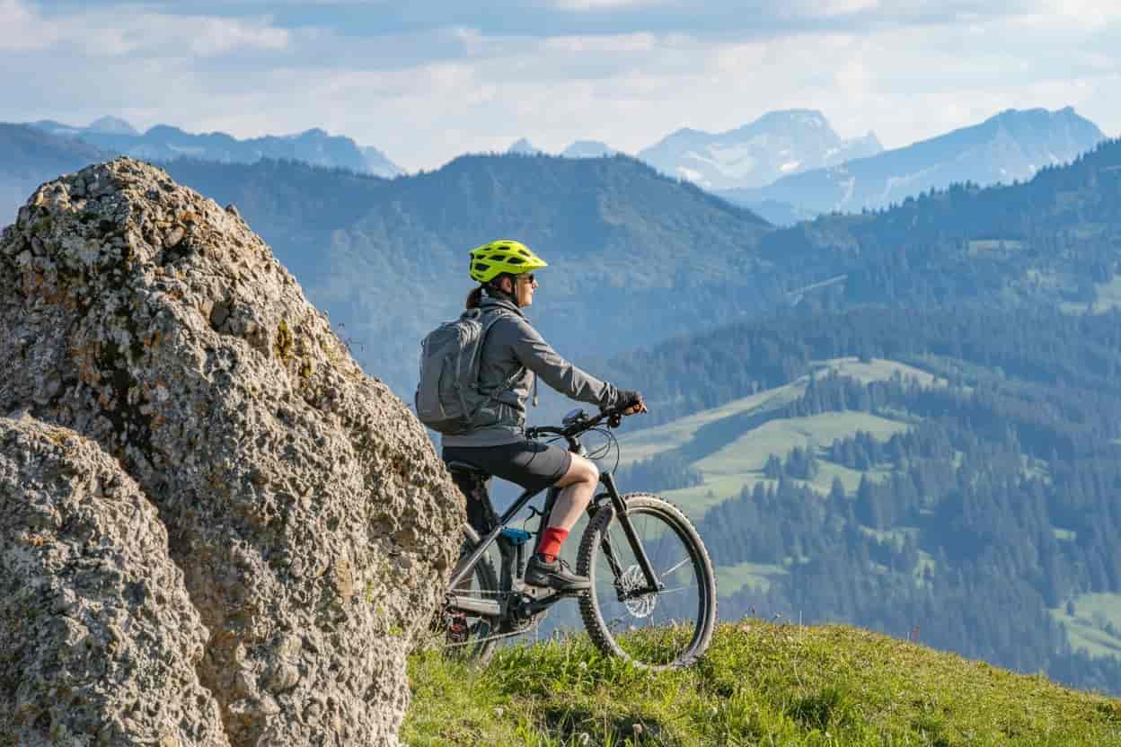 pretty senior woman riding her electric mountain bike in warm dawn sunlight and enjoying the spectacular view over the Allgau alps near Oberstdorf, Bavaria, Germany