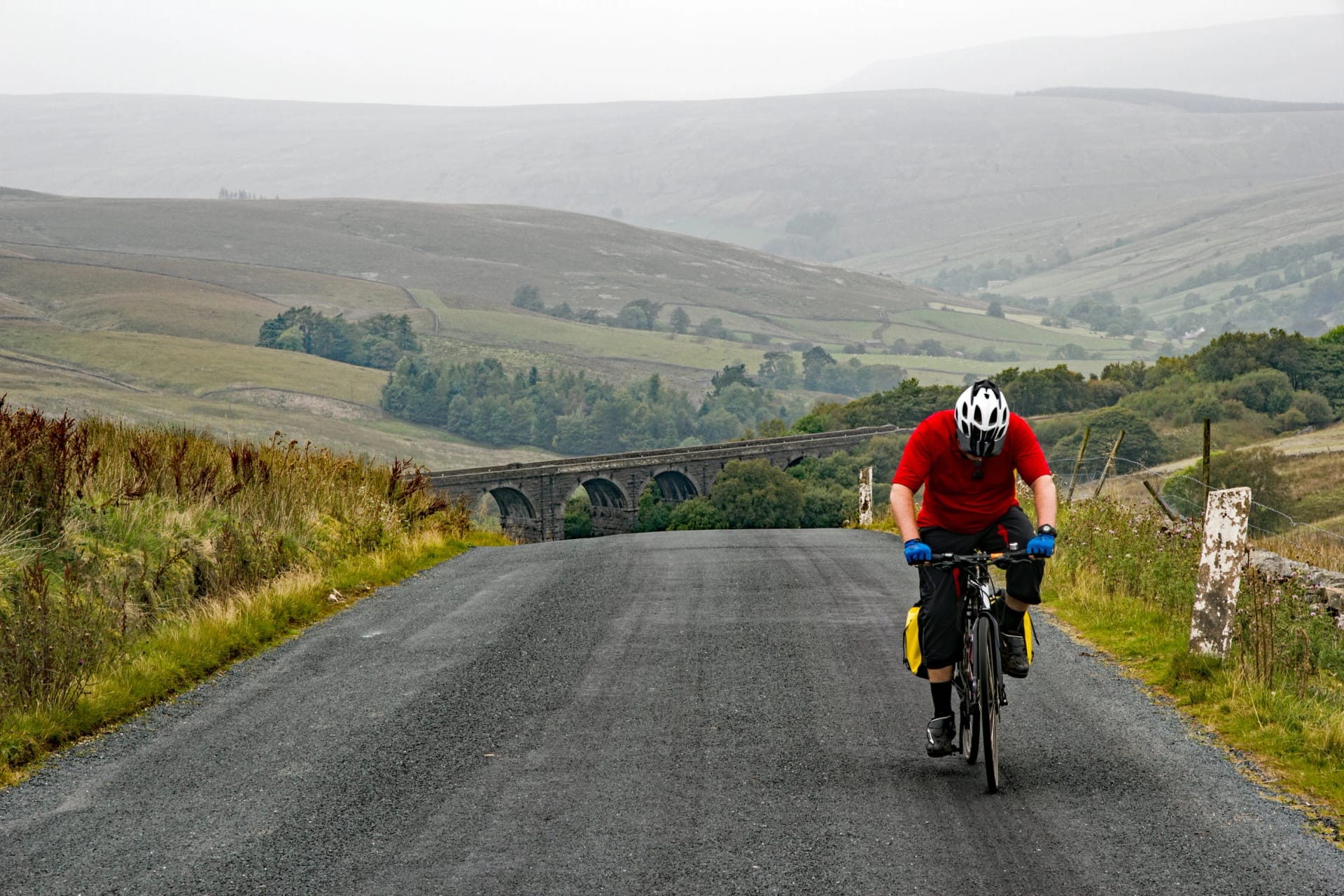 Cyclist pedals on after getting to the top of a very steep hill in the Yorkshire Dales National Park, UK