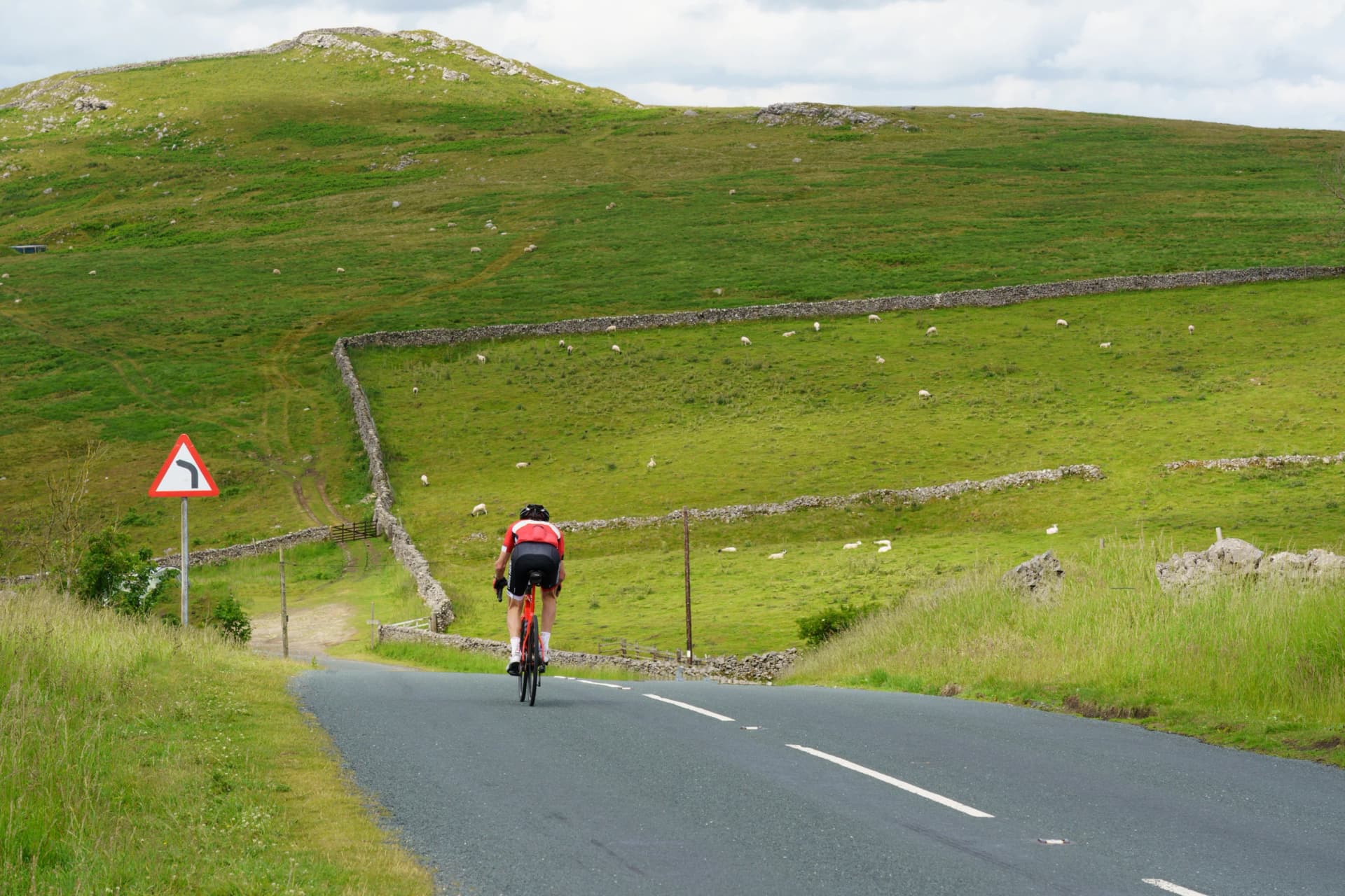 A male cyclist faces a big hill ahead of him on a scenic country road in the Yorkshire Dales, UK.