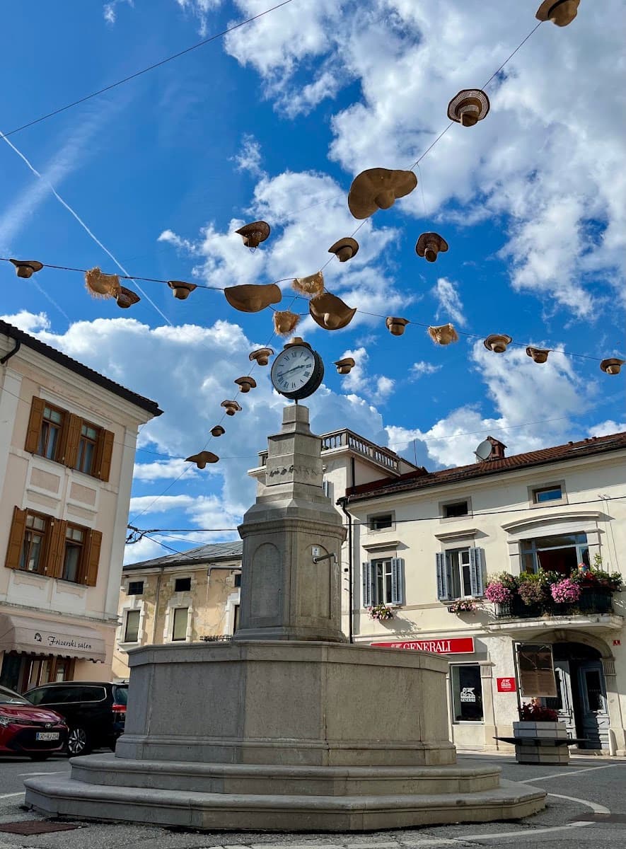 Stone fountain with clock and hanging straw hats in historic European town square