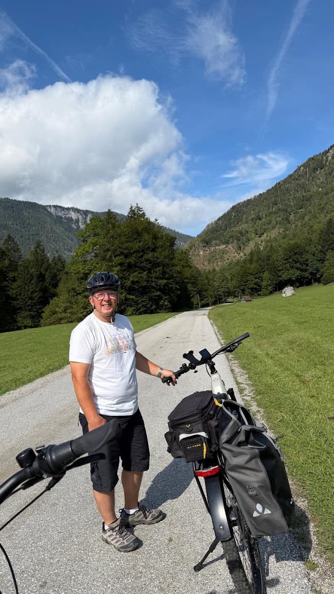 Cyclist with touring bicycle standing on a paved road through a mountain valley
