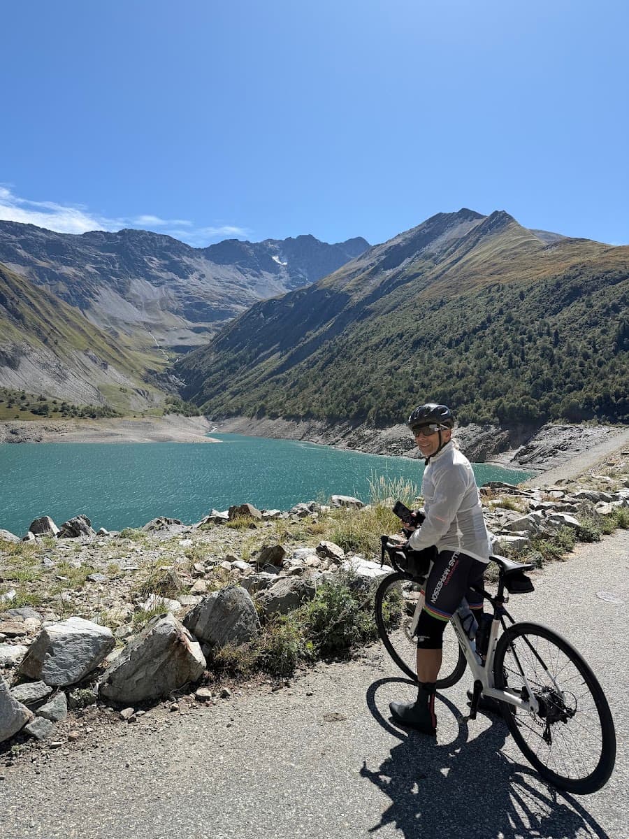 Cyclist on road beside alpine lake and mountains