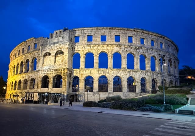 Roman amphitheater illuminated at night against a dark blue sky